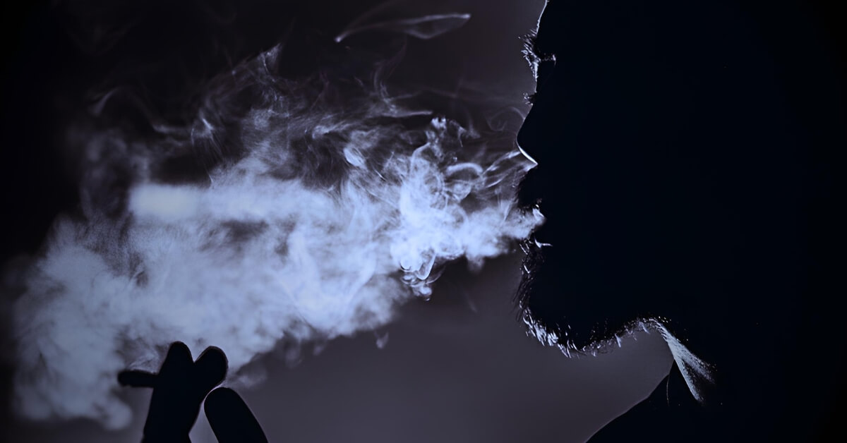 Black-and-white silhouette of a man exhaling smoke in a dark room, reflecting the quiet tension and mental strain associated with boredom in trading.