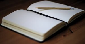 Open blank notebook with a wooden pencil on a wooden desk, symbolizing first-principles thinking and learning.
