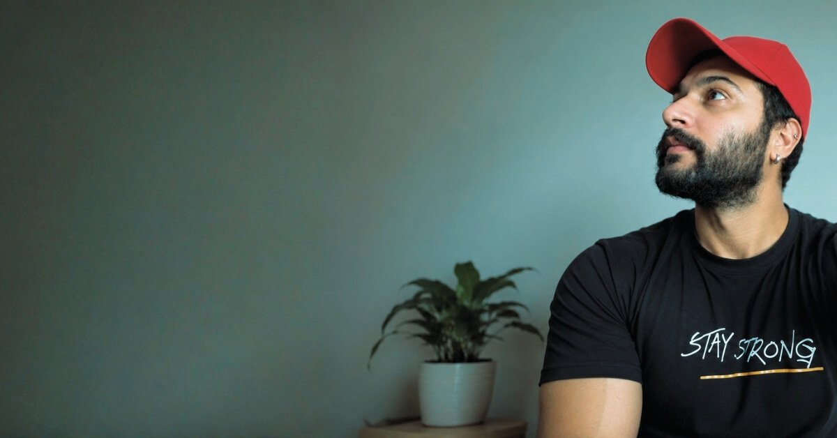 Hardeep Narula in a red cap and black Stay Strong T-shirt posing in a minimalist indoor setting.